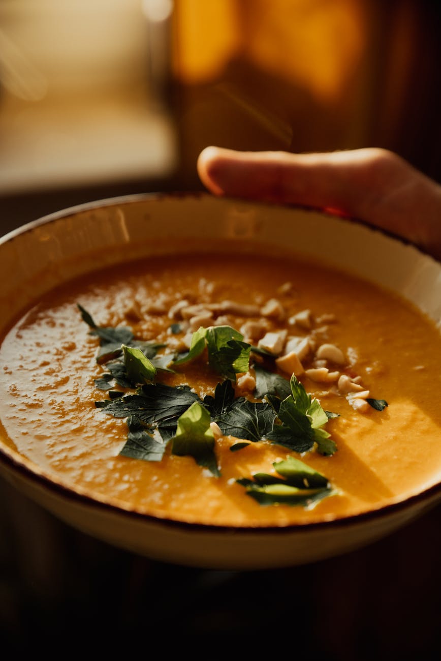 a hand holding a bowl of pumpkin soup